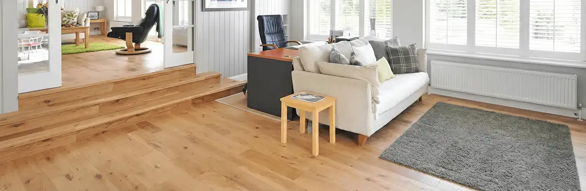 A modern living room with professionally installed laminate flooring, a beige sofa, a small side table, a gray rug, and large windows with white shutters in Kansas City, KS